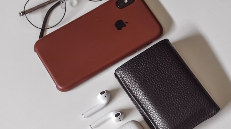 An iPhone beside a leather wallet, the physical wallet that Apple Wallet passes replace